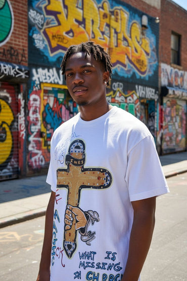 Man wearing a white t-shirt with a graphic design in an urban setting with graffiti.