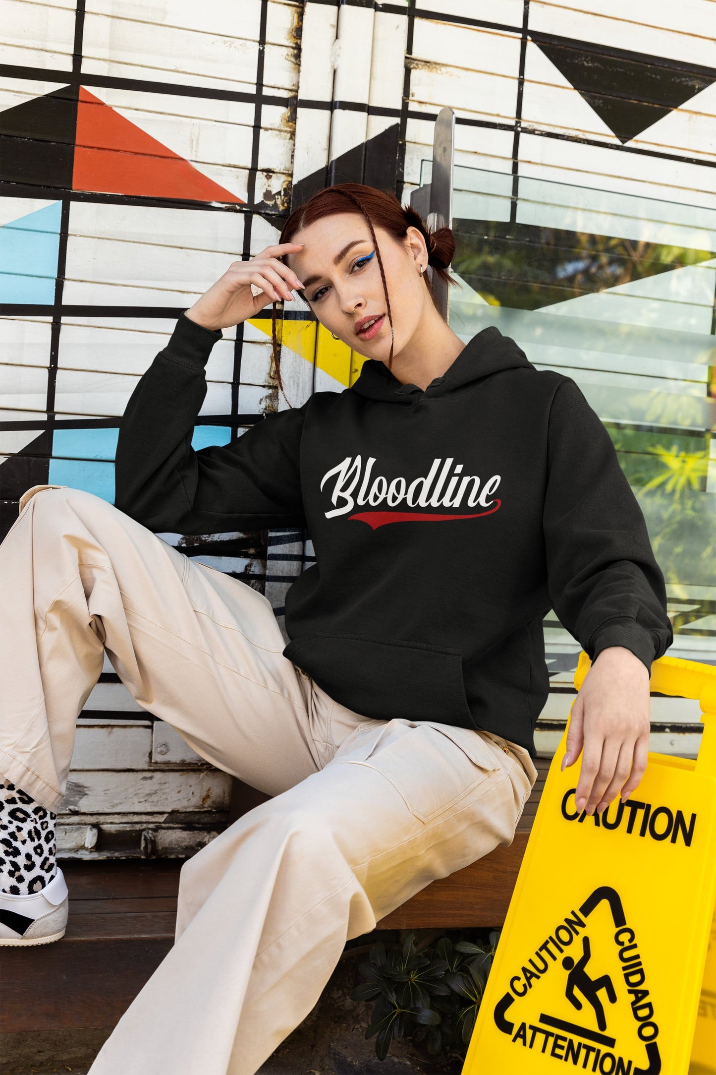 Person wearing a black hoodie with a logo, sitting against a colorful geometric wall.