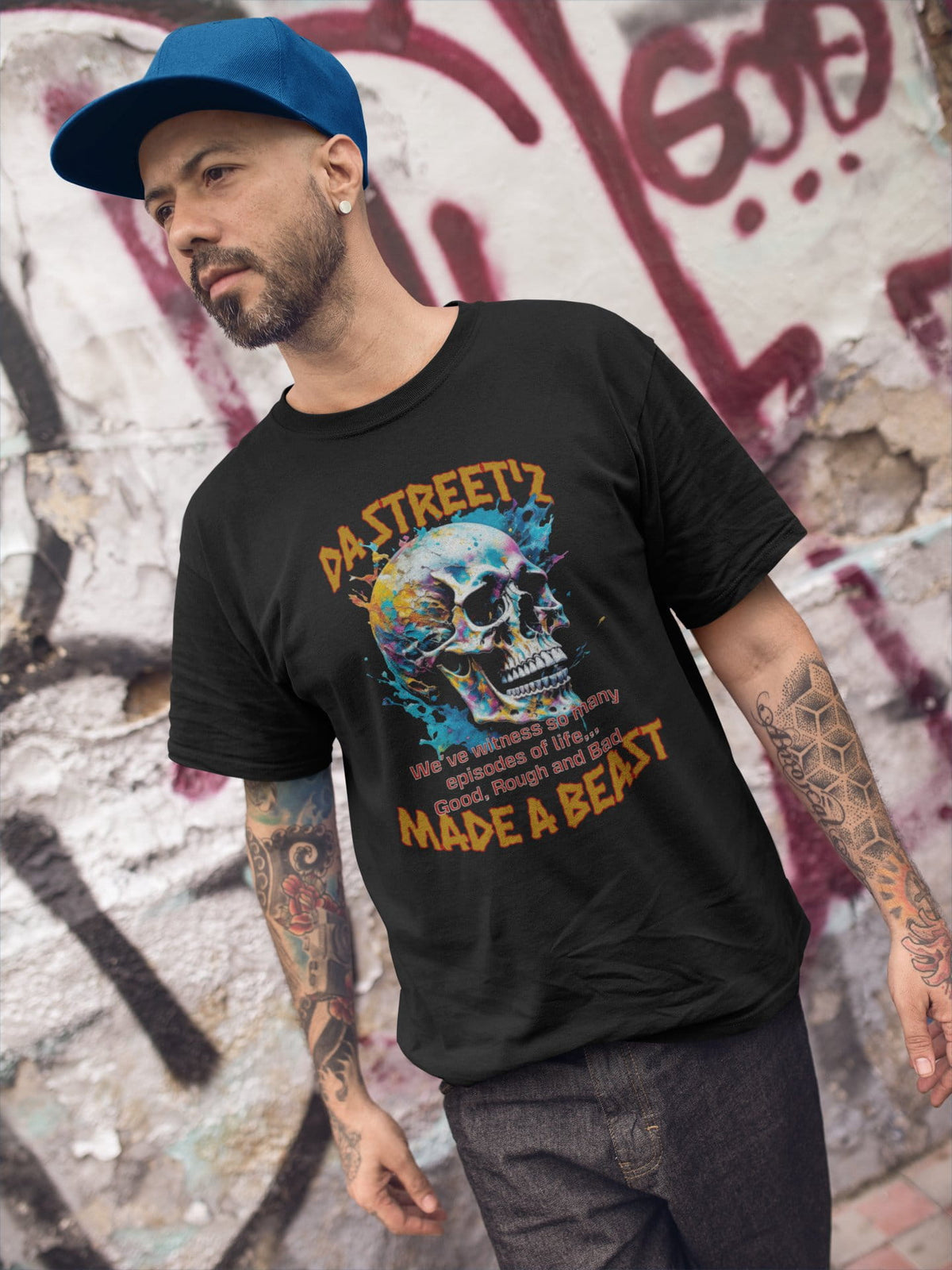 Man wearing a black t-shirt with a colorful graphic and text, standing against a graffiti-covered wall.