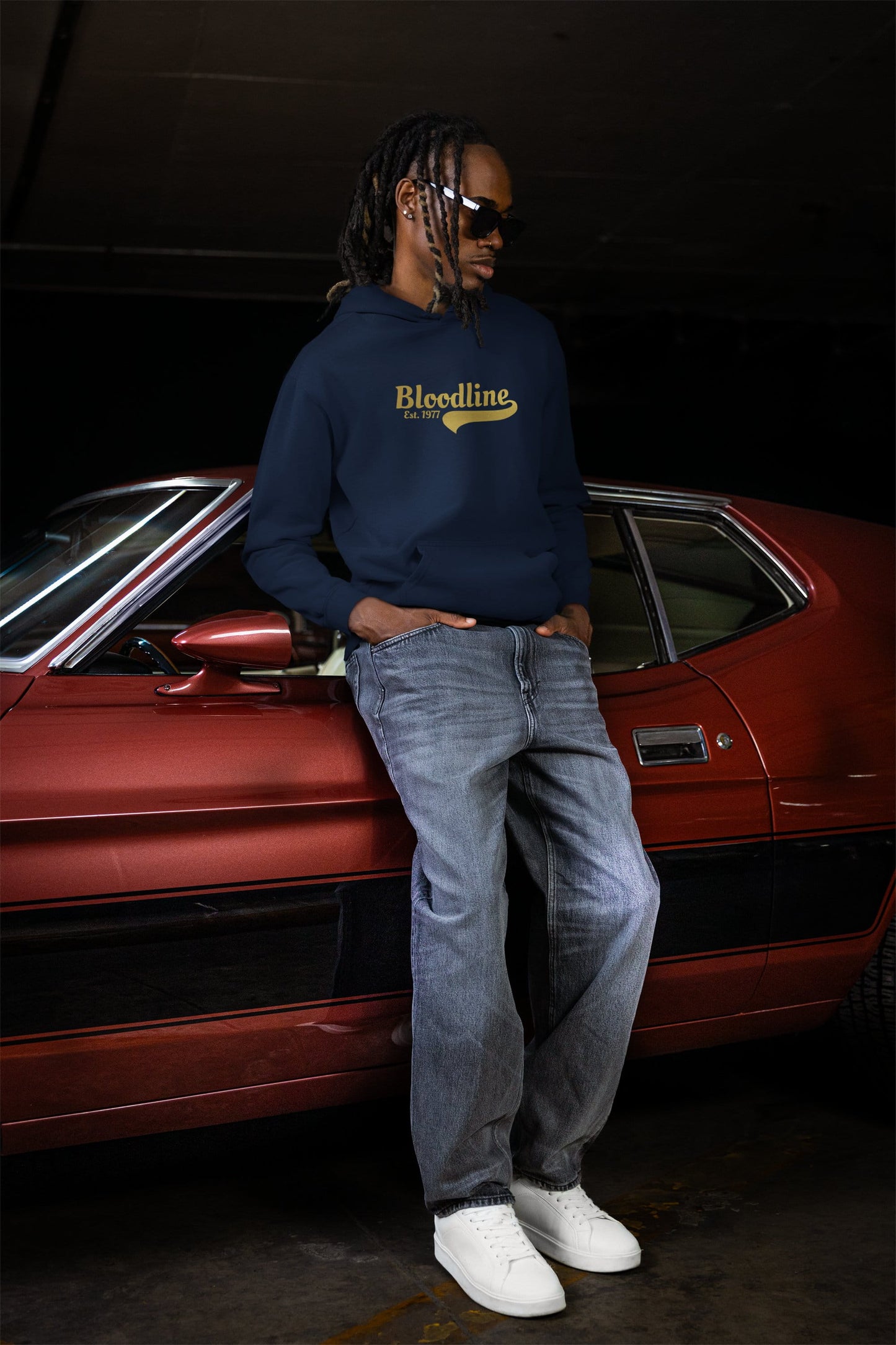 Person wearing a navy hoodie with 'Bloodline' text standing in front of a car on a black background