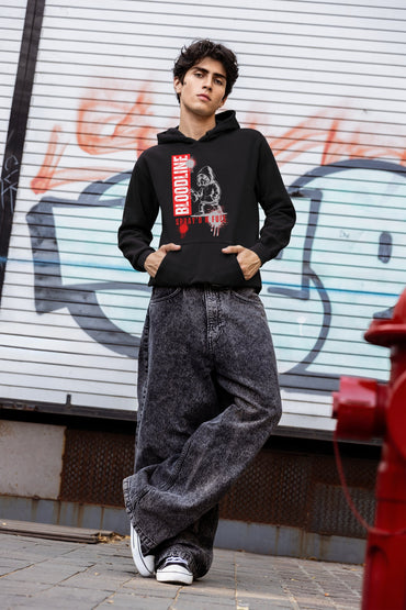 Man wearing a black hoodie with a graphic design, standing in front of a wall