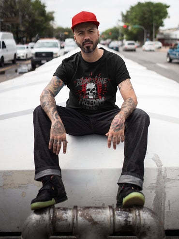 Man sitting on a car with tattoos and a red cap in an urban setting
