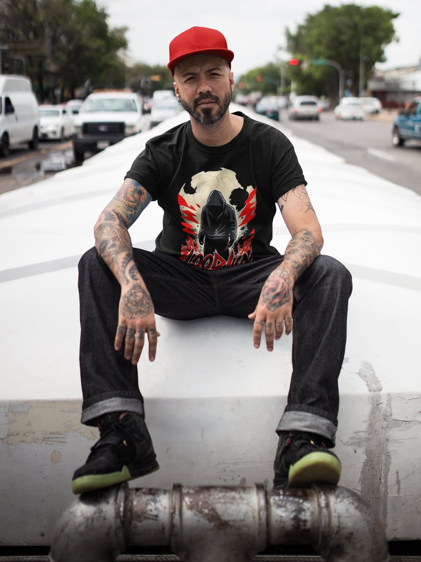 Man sitting on a car with tattoos and a red cap in an urban setting