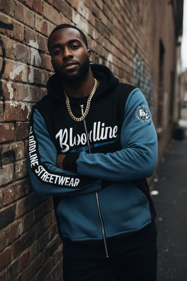 Man wearing a blue and black hoodie with 'Bloodline Streetwear' text against a brick wall.