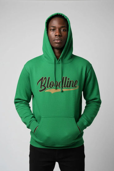 A man wearing a bright green pullover hoodie with 'Bloodline' printed across the chest in brown and gold, paired with black pants, against a neutral gray studio background.