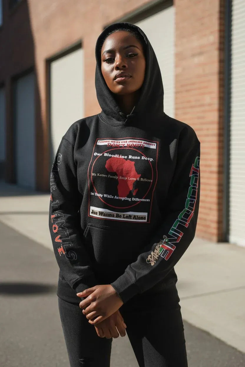 A person wearing a black pullover hoodie with a large red and white graphic on the chest and colorful text down the sleeves, standing outdoors in front of a brick building.