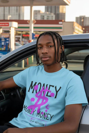 A young man with braided hair sits in a car, wearing a light blue graphic t-shirt with 'MONEY MONEY' and a pink dollar sign printed on the front.