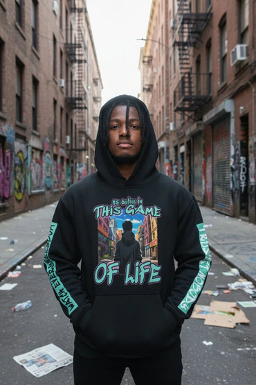 A man wearing a black pullover hoodie with a colorful graphic print on the chest and green text down the sleeves, standing in an urban alleyway.