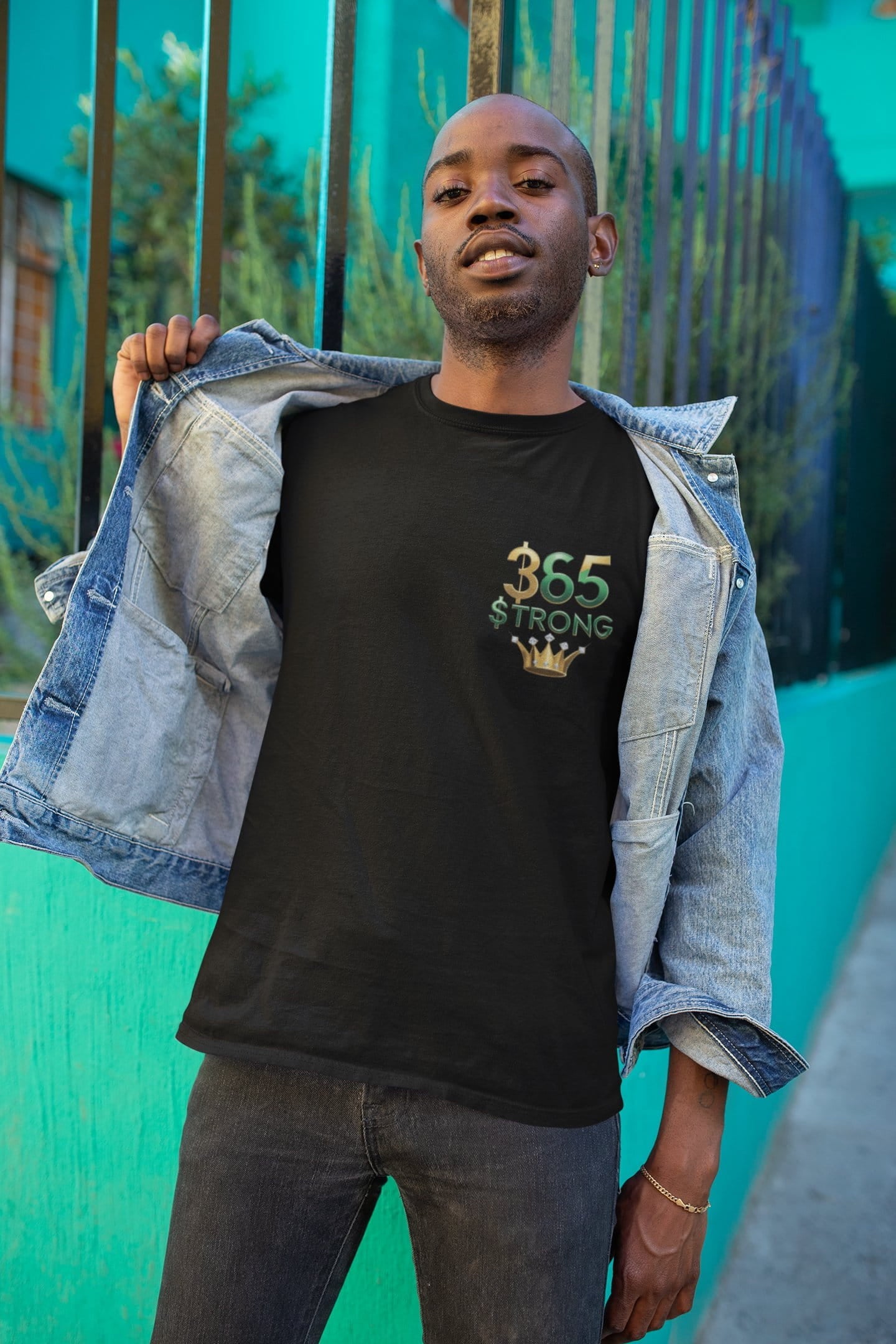 Man wearing a black t-shirt with '365 Strong' design, standing against a teal wall.