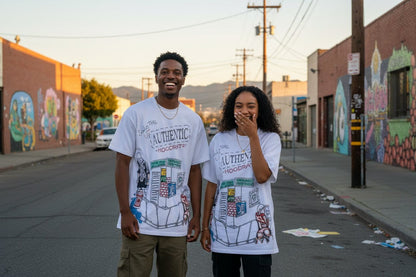 Two people wearing 'The Authentic' t-shirts on a street with murals.