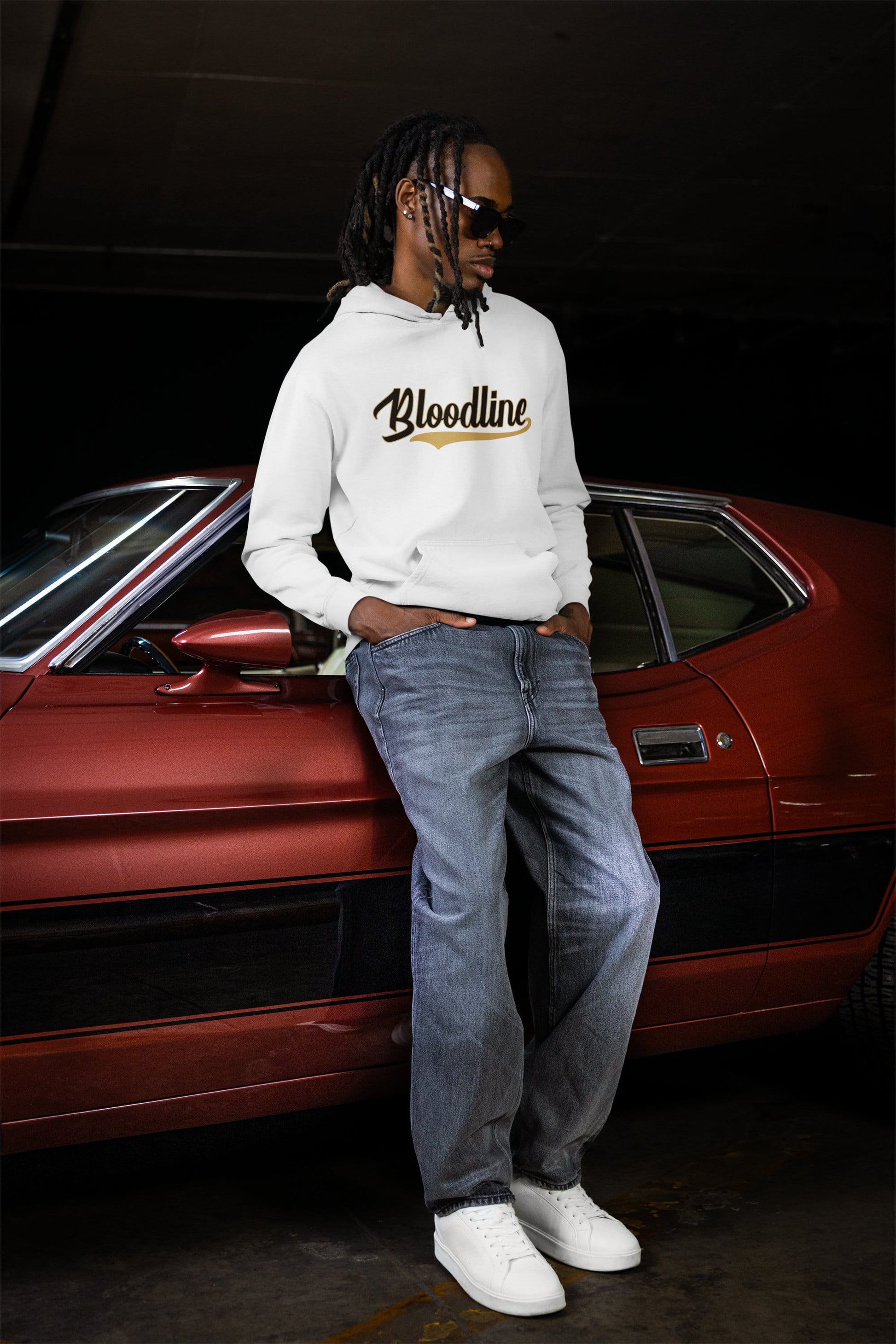 Person wearing a hoodie with 'Bloodline' text leaning against a red car.