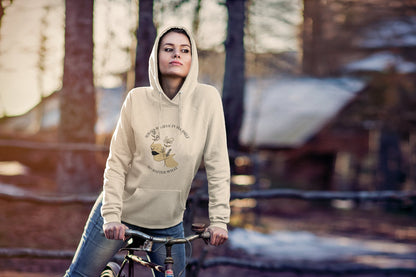 Person wearing a beige hoodie with a graphic design, standing next to a bicycle in a forest setting.