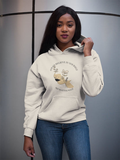 Woman wearing a beige hoodie with a motivational quote and graphic design on a gray background