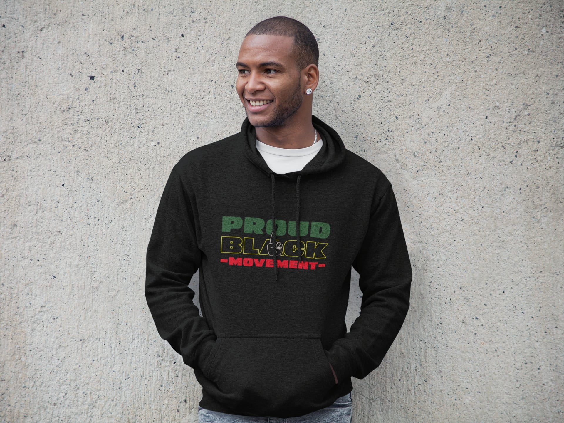 Man wearing a black hoodie with 'Proud Black Move Next' text against a concrete wall.