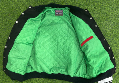 Green quilted jacket with black trim and red patch on a grassy background
