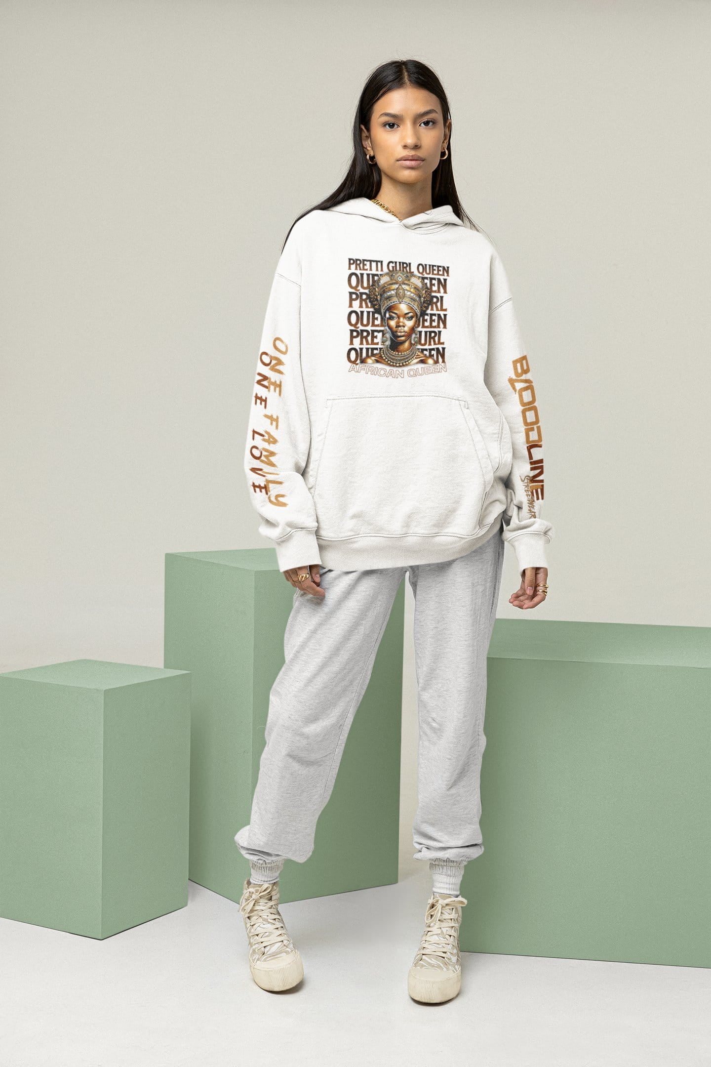 Person wearing a white hoodie with graphic design and text, standing in front of a green surface.