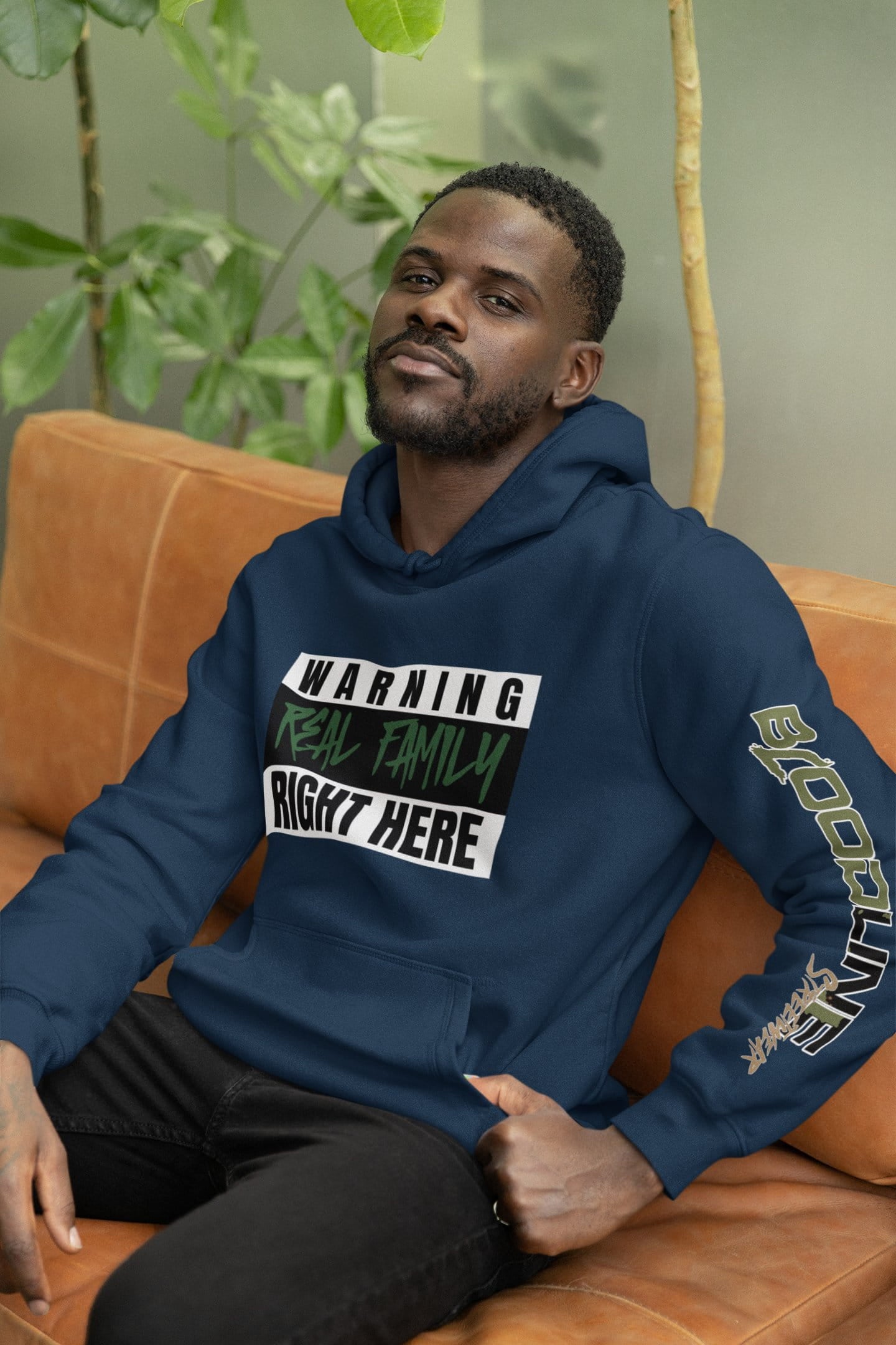 Man wearing a navy blue hoodie with text sitting on an orange couch.