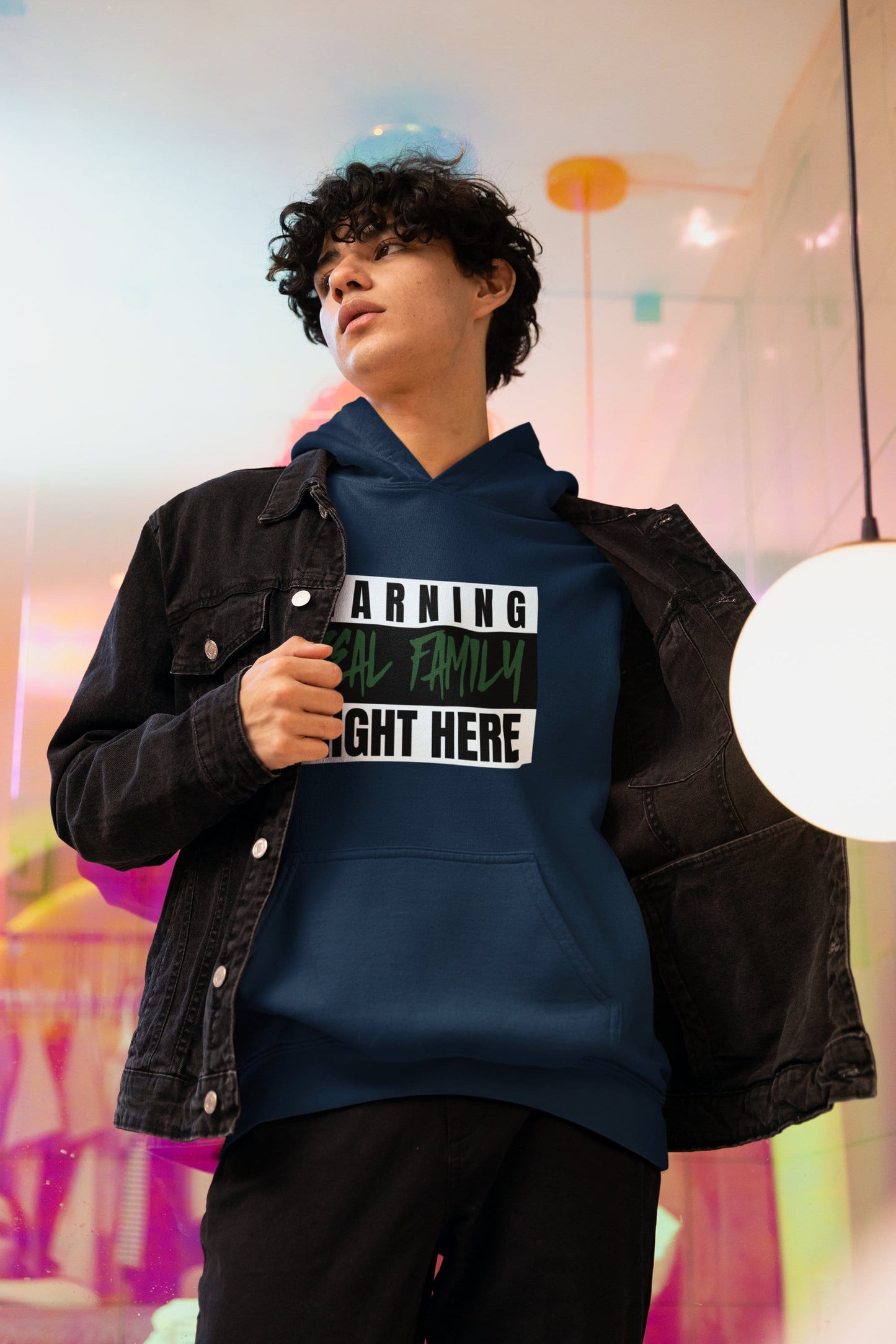 Person wearing a navy hoodie with text and a black jacket in a colorful indoor setting