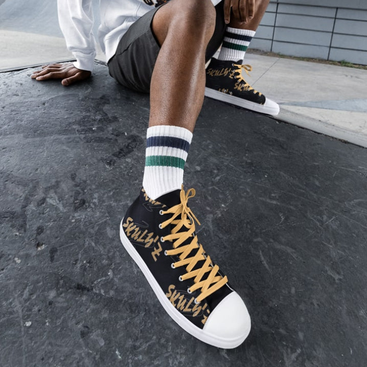 Person wearing a white sweatshirt with a tiger logo, black shorts, and black high-top Skuly'z sneakers with yellow accents.