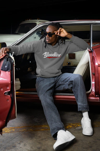 Man sitting in a red car wearing a gray sweatshirt with 'Bloodline' text.