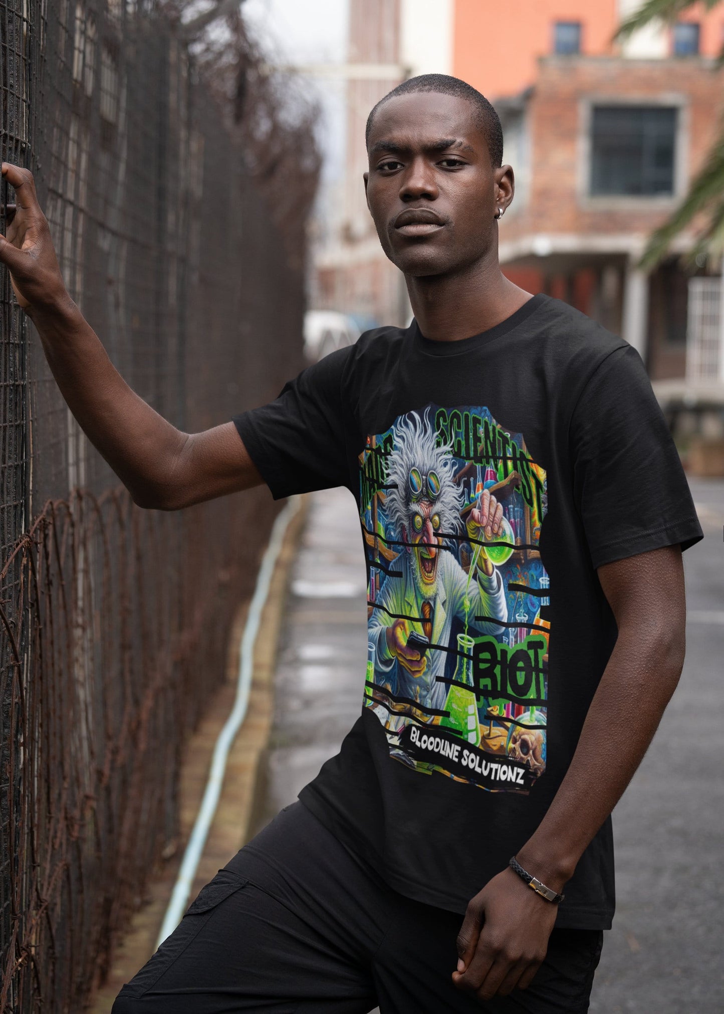 Man wearing a black t-shirt with colorful graphic design leaning against a fence.