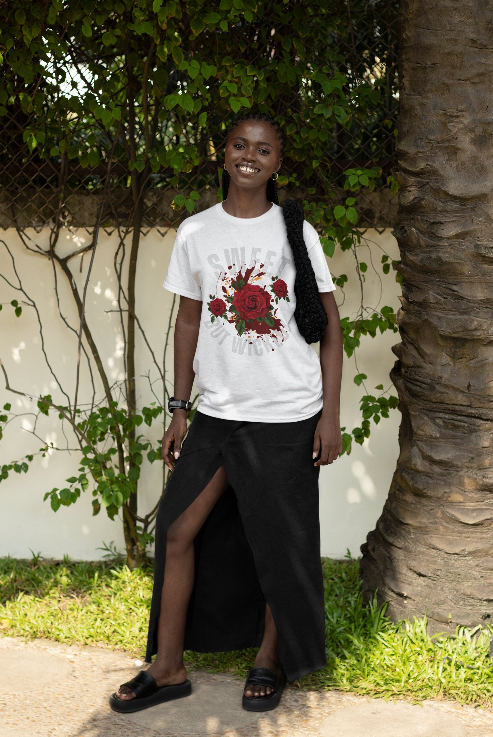 Person wearing a white t-shirt with a red floral design and a black skirt standing outdoors.