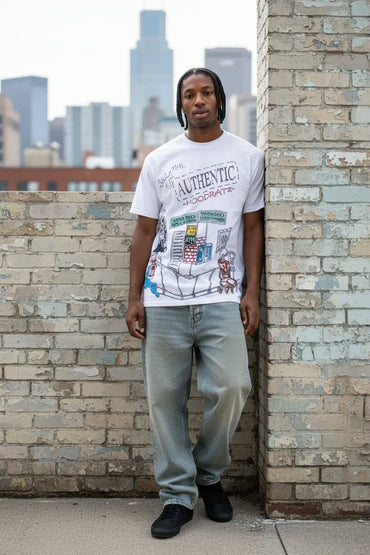 A man wearing a white graphic t-shirt and light-wash jeans stands against a brick wall with a city skyline in the background.