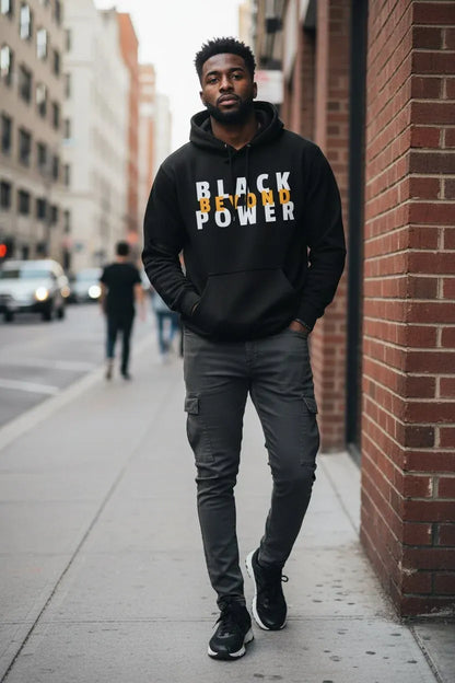 A man walking on a city sidewalk wearing a black pullover hoodie with 'BLACK POWER' printed across the chest in white and yellow, paired with dark gray cargo pants and black sneakers.