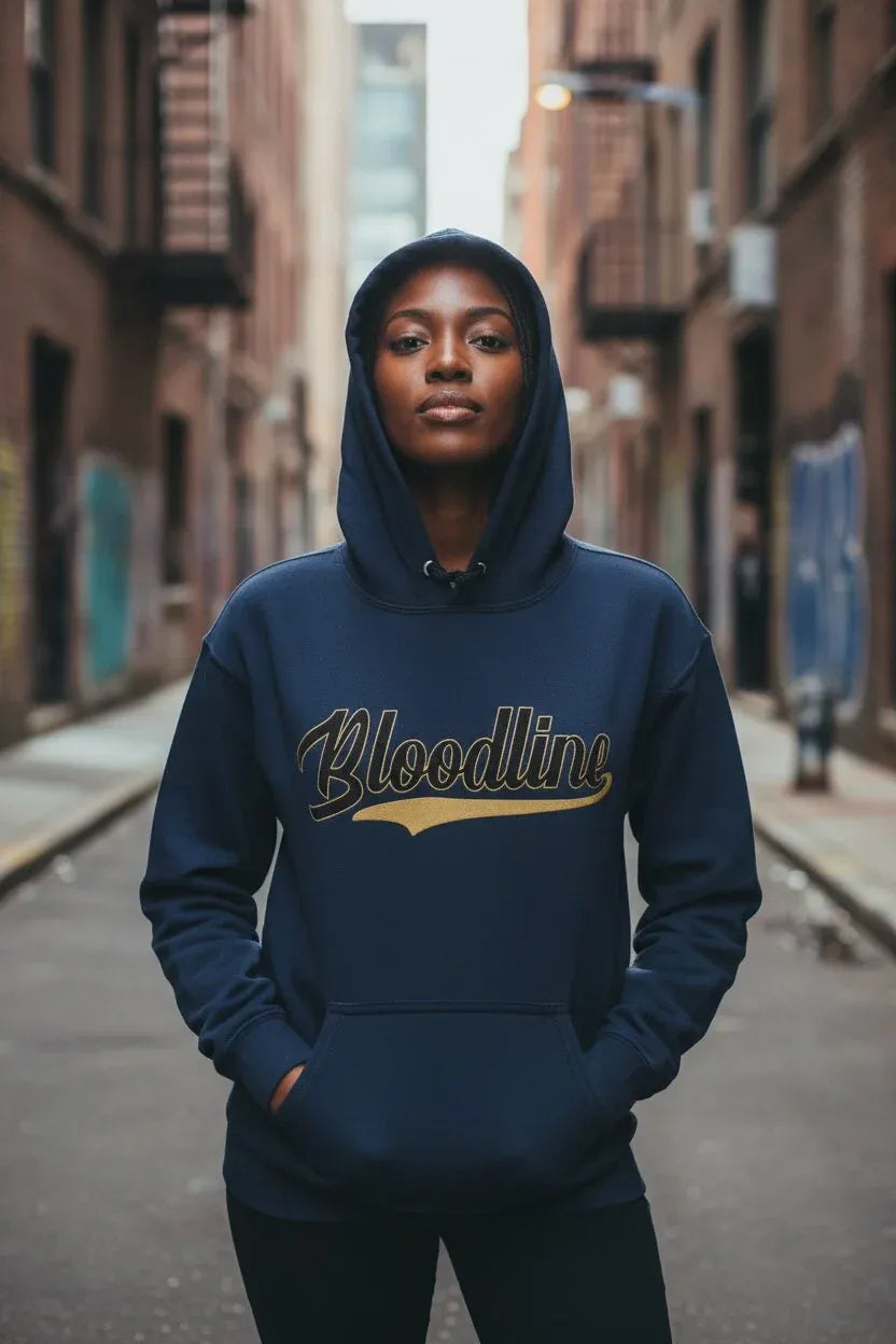 A woman wearing a navy blue hoodie with 'Bloodline' printed across the chest in gold and black, standing in a narrow urban alleyway.