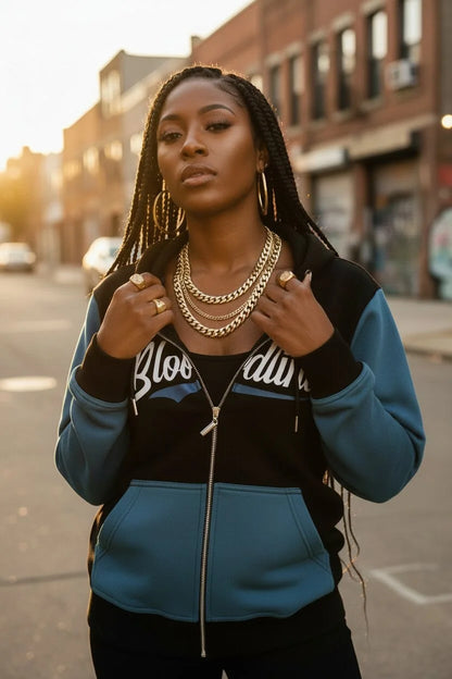 Woman wearing a blue and black jacket with gold jewelry on a city street.