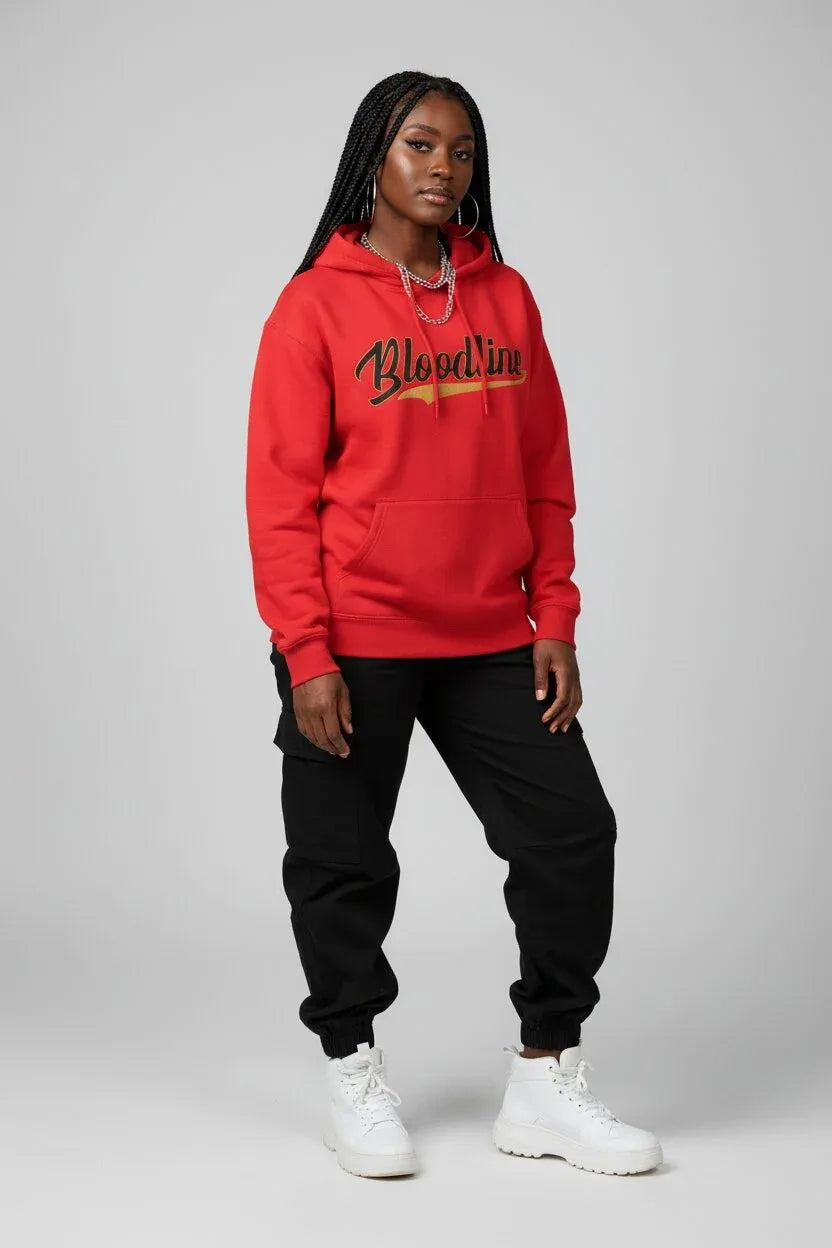 A woman modeling a bright red hoodie with 'Bloodline' printed across the chest in black and gold, paired with black jogger pants and white sneakers, against a light gray studio background.