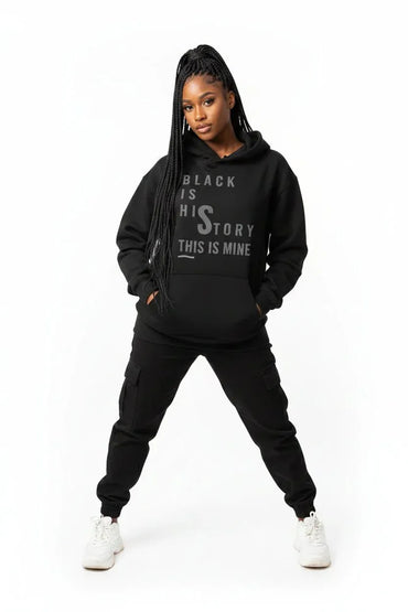 Black female model wearing the Bloodline Streetwear "This Is Mine" black hoodie, full body front view, white studio background