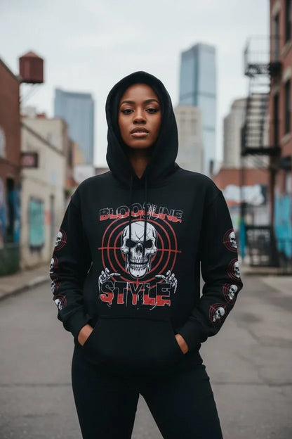 A woman wearing a black pullover hoodie with a large red and white skull graphic and the words 'BLOODY STYLE' on the front, standing in an urban alleyway.