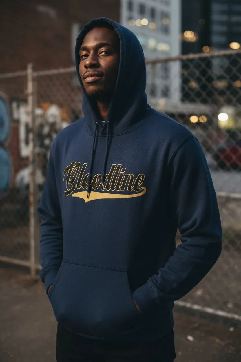A man wearing a navy blue hoodie with 'Bloodline' printed across the chest in gold and black, standing outdoors in front of a chain-link fence at night.
