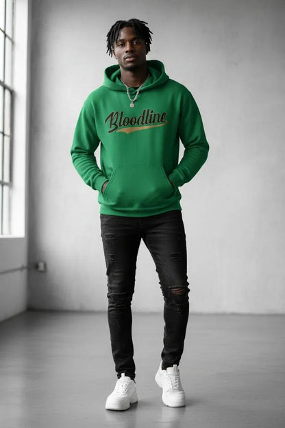 A man wearing a bright green hoodie with 'Bloodline' printed in black script and gold across the chest, paired with black ripped jeans and white sneakers, standing in a minimalist gray room.