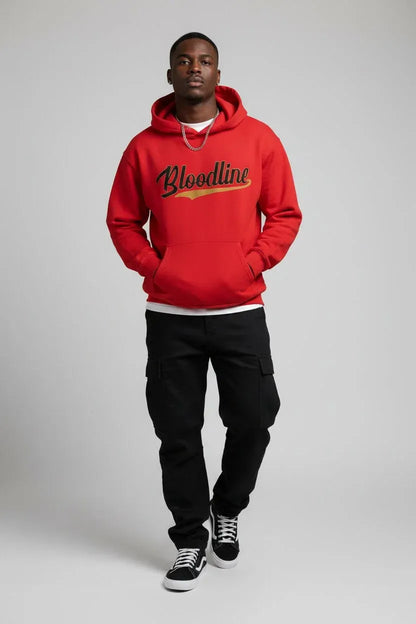 A man modeling a bright red pullover hoodie with 'Bloodline' printed across the chest in black script with a gold outline, paired with black cargo pants and black sneakers, shot against a neutral gray studio background.