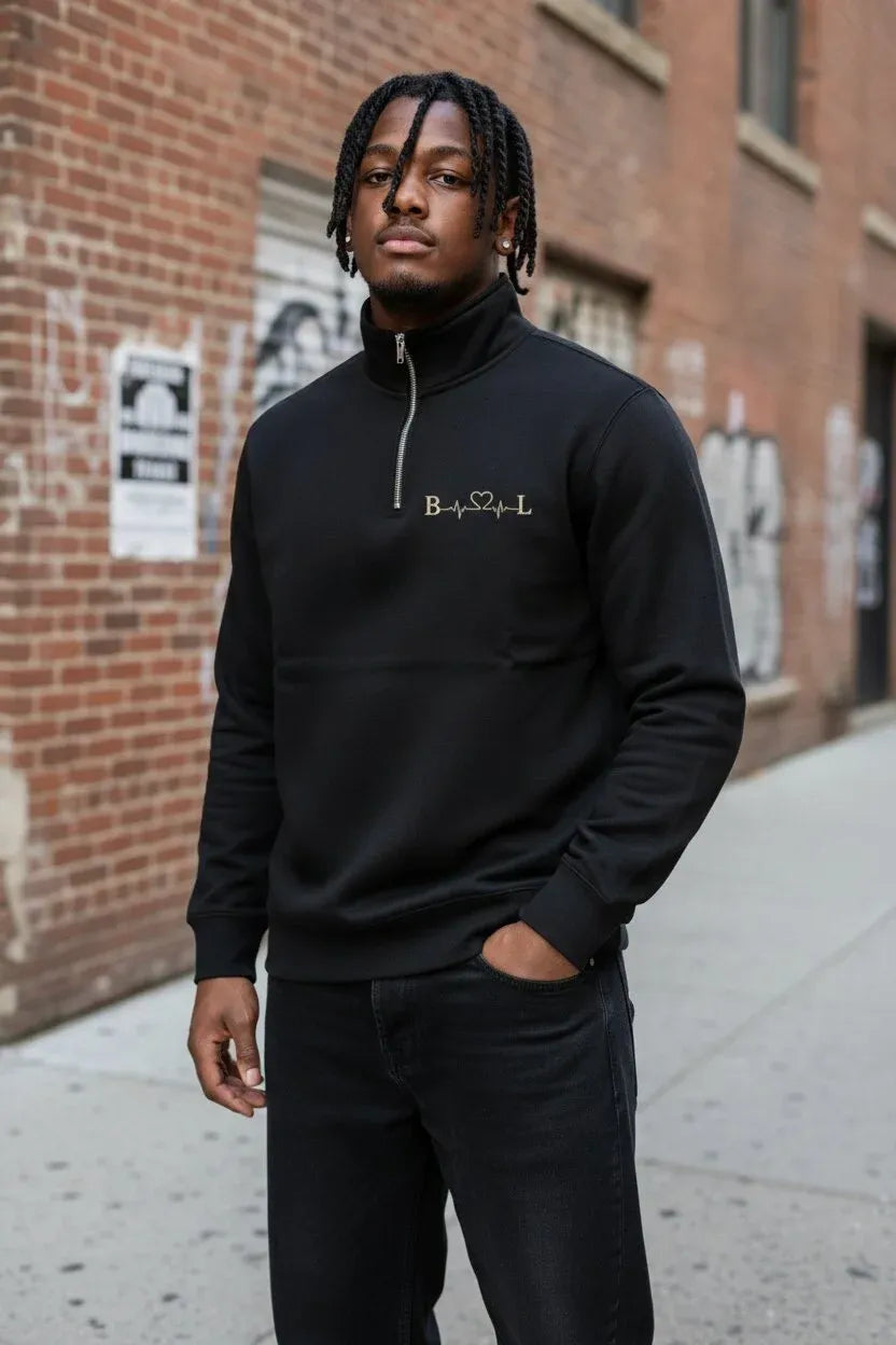 A man wearing a black quarter-zip sweatshirt with a gold 'B.S.