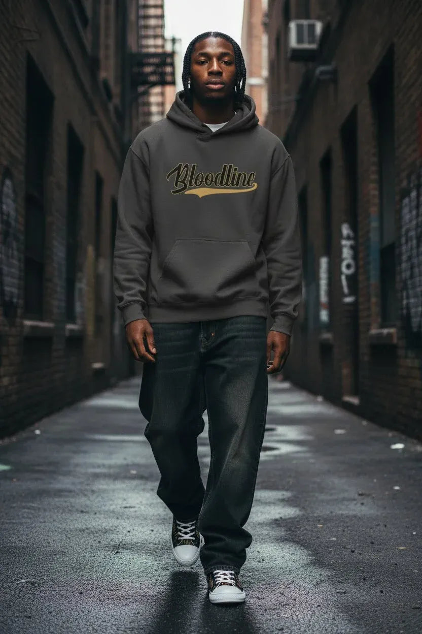 A man wearing a dark gray hoodie with 'Bloodline' printed in gold script across the chest, walking down a wet city alleyway.