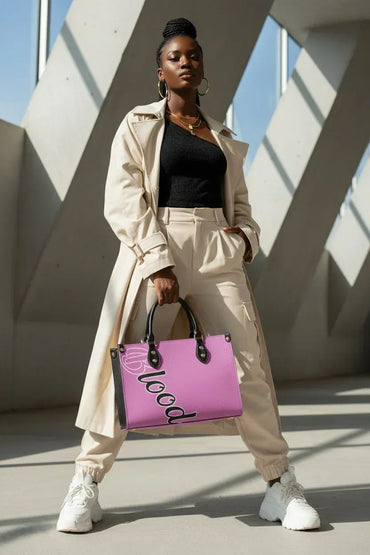 A woman stands in a modern architectural setting with concrete beams, holding a bright pink tote bag with black handles and the word 'LOVE' printed on it. She is wearing a beige trench coat, beige pants, a black top, and white sneakers.