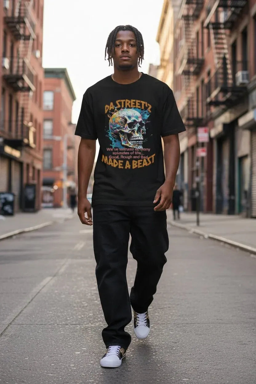 A man walking down an urban city street wearing a black graphic t-shirt with a colorful skull design and the text 'DA STREETS MADE A BEAST', paired with black pants and white sneakers.