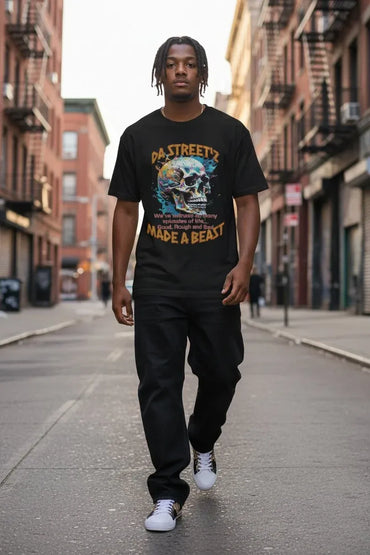 A man walking down an urban city street wearing a black graphic t-shirt with a colorful skull design and the text 'DA STREETS MADE A BEAST', paired with black pants and white sneakers.