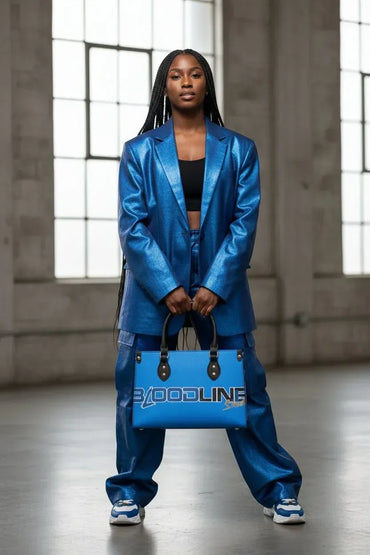 A model stands in a warehouse setting wearing a shiny metallic blue blazer and matching pants, holding a blue tote bag with the brand name 'XOODLINE' printed on it.