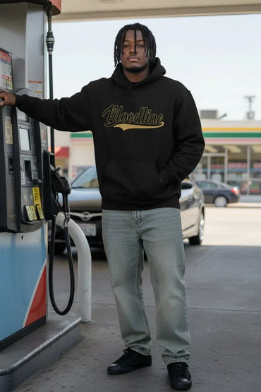 A man standing at a gas pump wearing a black hoodie with 'Bloodline' printed in gold script across the chest, paired with light gray jeans and black sneakers.