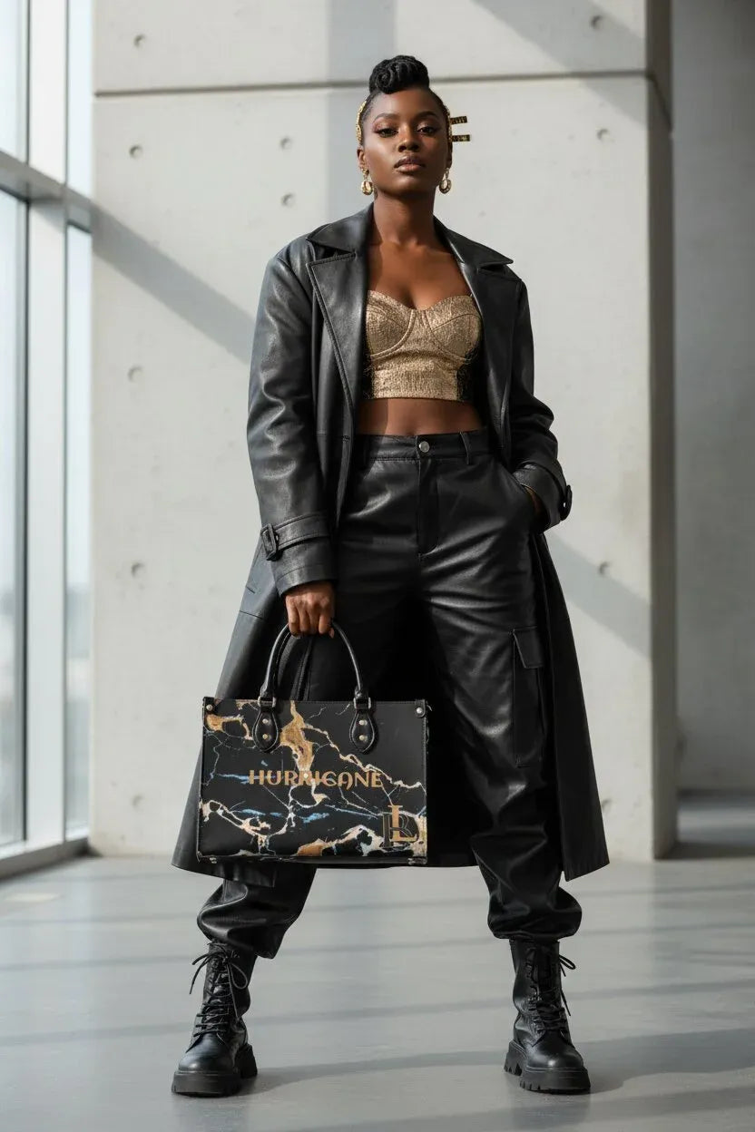 A model stands in a minimalist concrete hallway wearing a long black leather coat, black leather pants, and black combat boots, while holding a black and gold marbled tote bag with the brand name 'HUB & GONE' printed on it.