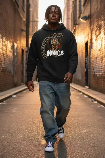 A man walking down a brick alley wearing a black hoodie with a graphic print that reads 'BLOODLINE INFAMOUS' and a tiger illustration, paired with blue jeans and black-and-white sneakers.