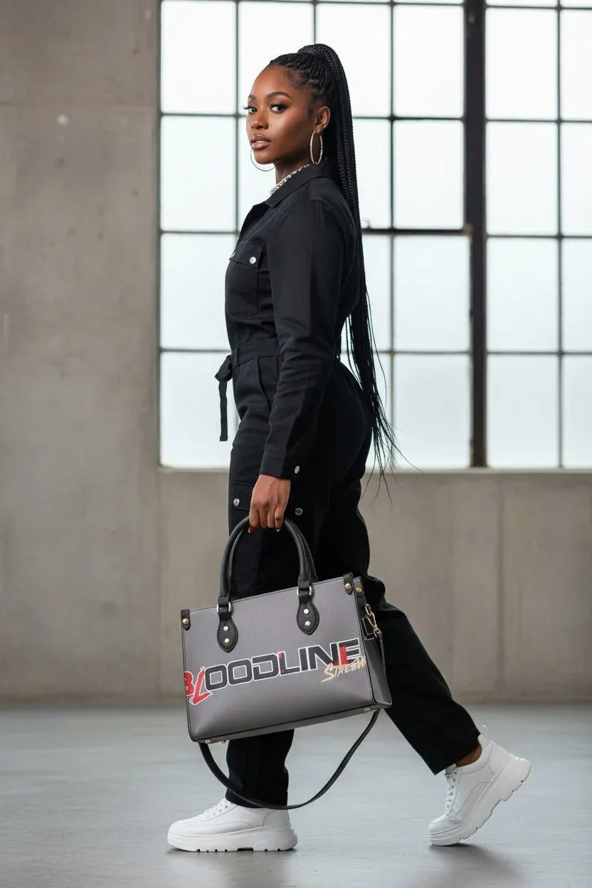A woman in a black jumpsuit and white sneakers carries a gray tote bag with 'VOODLINE' printed in red and white on the front, walking in a modern industrial loft setting.