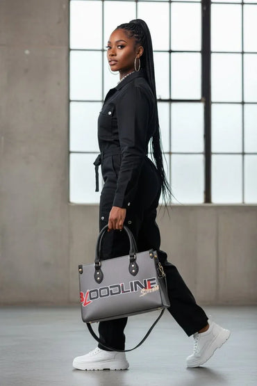 A woman in a black jumpsuit and white sneakers carries a gray tote bag with 'VOODLINE' printed in red and white on the front, walking in a modern industrial loft setting.