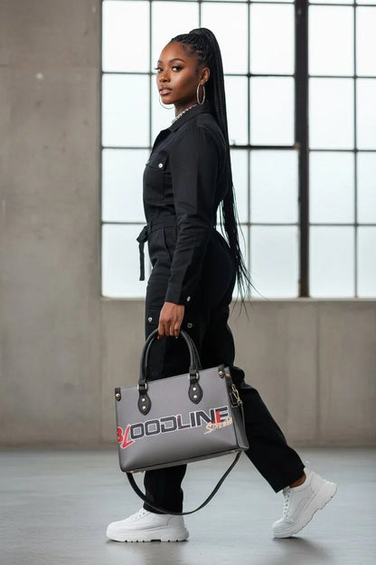 A woman in a black jumpsuit and white sneakers carries a gray tote bag with 'VOODLINE' printed in red and white on the front, walking in a modern industrial loft setting.