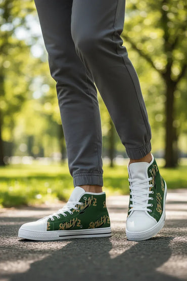 A person wearing dark gray jogger pants and green high-top sneakers with gold graffiti-style lettering, standing on a paved path in a sunny park.