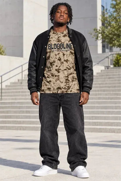 A man wearing a black leather bomber jacket over a beige and black camouflage t-shirt with 'BLOODLINE' printed on the chest, paired with dark gray jeans and white sneakers, standing on outdoor concrete steps.